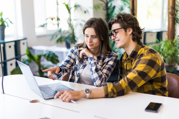 Beautiful young business woman and man are using a laptop, discussing documents and smiling while working in office