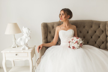 Young bride in a beautiful dress sitting at home with nice white interior. Wedding concept.