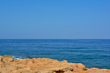 view from a stone cliff to the blue sea against a cloudless blue sky