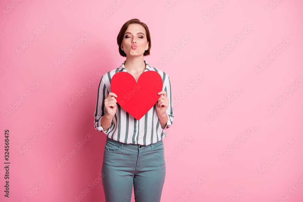 Wall mural Portrait of positive charming girl have 14-february date send air kisses to her boyfriend she get red big paper card heart wear grey stylish trousers isolated over pink color background