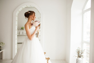 Young bride in a luxury dress holding a bouquet of flowers in bright white studio. Wedding fashion concept.