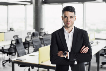 Handsome young businessman in office. Cheerful self confident professional man with crossed hands portrait. Business success concept