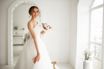 Young bride in a luxury dress holding a bouquet of flowers in bright white studio. Wedding fashion concept.