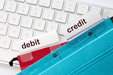 tow hanging folders on in red and in blue on a keyboard having tabs with the words debit and credit on it