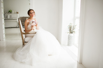 Fototapeta na wymiar Young bride in a luxury dress holding a bouquet of flowers in bright white studio. Wedding fashion concept.