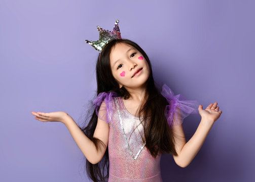Cute asian kid girl princess in party dress and crown and with painted red hearts is holding hands up with open palms