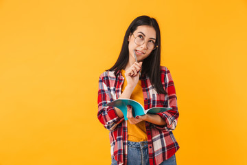 Photo of thinking brunette woman smiling while making notes in diary
