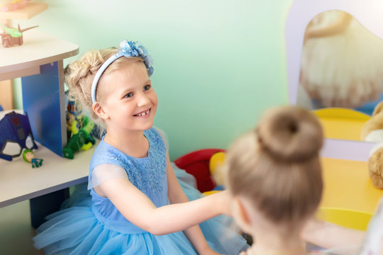 Cute adorable blond caucasian happy little girl in beautiful blue dress and headband enjoy playing and speaking with friend at kindergarten party indoor. Children celebration event