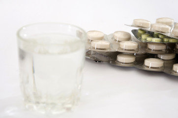 pills in a blister pack a glass of water on white. Health concept.