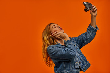 Woman with wavy hair in a denim jacket with photo camera in her left hand.