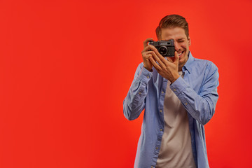 Smiling man with a beard in a blue shirt takes a photo on old photo camera.