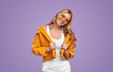 Joyful millennial woman in trendy outfit on lilac background