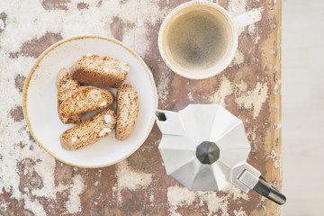 Cantucci, typical Italian dry almond biscuits and a cup of morning coffee over rustic wooden background with moka pot. Top view