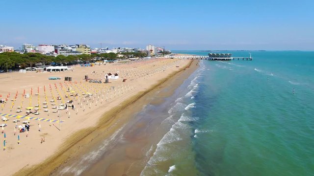 Sea waves gently lapping on the wide sandy beach Lignano Sabbiadoro, Italy. Aerial dolly wide shot
