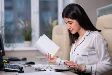 Fototapeta premium Portrait of a young beautiful woman, an office employee in a white shirt. A woman works at a computer.