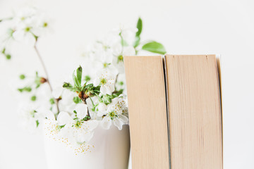 Books and flowers in vase.White minimalistic background.Copy space.