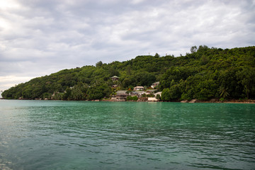 Fototapeta na wymiar Seychelles islands shore line. Green water and cloudy sky