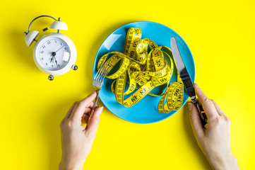 fist on a plate with a measuring tape. Alarm clock. Woman hands hold fork and knife