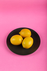 Yellow lemons in a black plate on a pink background