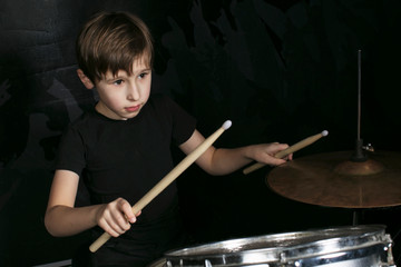 The child behind the drum. A boy with drumsticks behind a drum kit.
