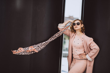 Elegant fashion. Stylish blonde woman in pink clothes and sunglasses posing in the city on a background of black huge barrels. Soft selective focus. Copy space.