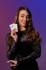 Brunette woman in black velvet dress showing two playing cards, posing against coloful background. Gambling entertainment, poker, casino. Close-up.