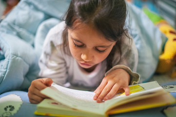 child in bed reading a book before bed