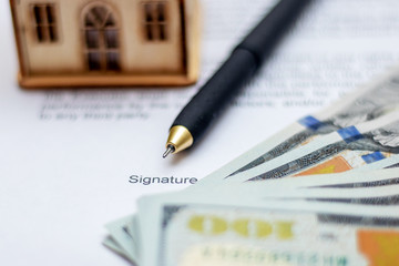 Fototapeta premium Handle for signing a document on the sale and purchase of a house. Model of the house near the money and the document on the purchase of housing_
