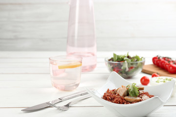 Tasty brown rice with meat and vegetables on white wooden table