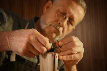 Man sewing piece of leather in workshop, closeup