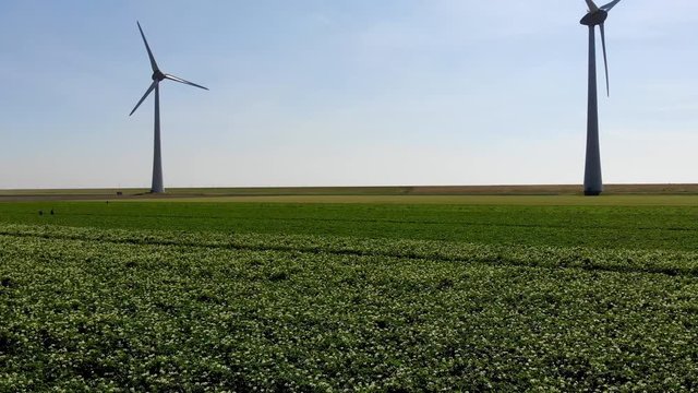Aerial view of modern windmills with rotating propeller standing in rural farmland agri meadow. Wind blowing generating renewable energy for clean resources. Electric power production