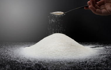 Spoon in sugar on a black background. The concept of addiction to sweets. Macro photo of granulated...