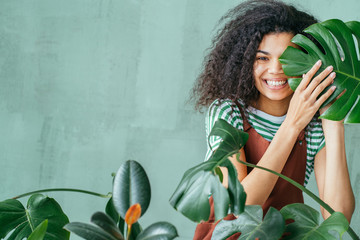Young woman with natural make up and tropical monstera leaf in hand over green background with copy space. Skin care, pure beauty, body treatment, cosmetics concept. © Iryna