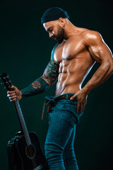 Strong and fit man bodybuilder with guitrar shows abdominal muscles. Sporty muscular guy athlete. Sport and fitness concept. Men's fashion.