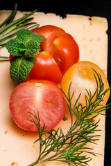 Ripe sliced ​​tomatoes with mint, basil, on a slice of cheese and a black background close-up