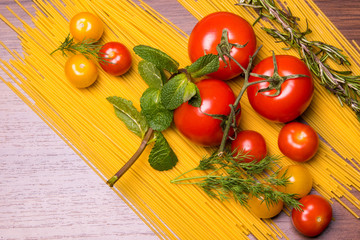Ripe tomatoes and cherry with mint rosemary and dill on spaghetti on a wooden background