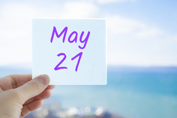 May 21st. Hand holding sticker with text May 21 on the blurred background of the sea and sky. Copy space for text. Month in calendar concept