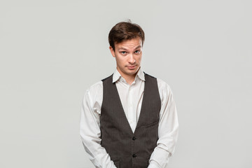 Young man in a white shirt and grey vest in high dudgeon over grey background