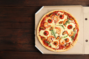 Delicious seafood pizza in cardboard on wooden table, top view. Space for text