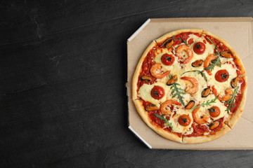 Delicious seafood pizza  in cardboard box on black table, top view. Space for text