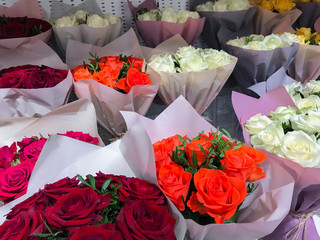 Many bouquets of different colored bright roses-red, orange, white, yellow in pink packaging paper are sold in the flower sho
