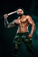 Fototapeta na wymiar Strong and fit man bodybuilder with baseball bat shows abdominal muscles under a t-shirt. Sporty muscular guy athlete. Sport and fitness concept. Men's fashion.