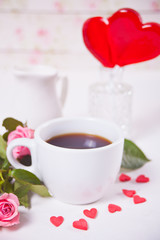 Red heart shape candies lollipops with cup of coffee and roses on the background.