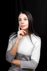 Closeup portrait of a thoughtful pretty confident girl, holding the hand near the face, looking earnestly up, standing over black background with copy space