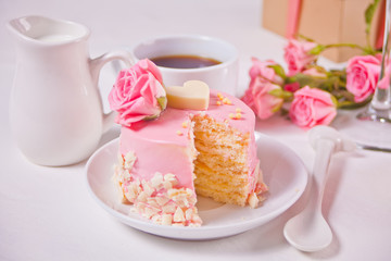 Mini small cake with pink glaze, beautiful roses, cup of coffee, gift box on the white table.