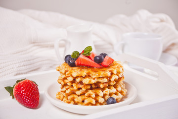 Plate with sweet tasty waffles with honey and berries. Cup of tea and teapot on the background.
