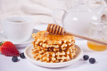 Plate with sweet tasty waffles with honey, berries, cup of tea on the white background.