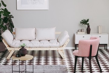 Pastel pink armchair and beige scandinavian futon in trendy living room interior with black and white floor