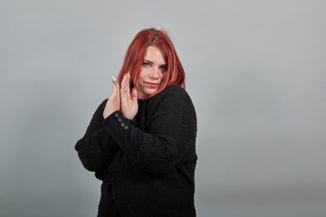 Young redhead fat girl in black sweater on grey background a dissenting woman shows her arms...