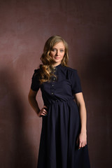 Vertical image of smiling woman pointing up and looking at camera while holding arm in pocket and posing near the wall in studio over gray background
